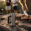 Beer Stein Stainless steel beer stein placed beside a braai grill with steaks cooking outdoors, showcasing a rugged beer mug ideal for South African braais and gatherings.