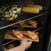 Masterbuilt Dual Fuel Smoker Braai - With Gas and Charcoal Grill Fresh salmon fillets with lemon and vegetables placed inside a smoker braai for wood-smoked flavour.